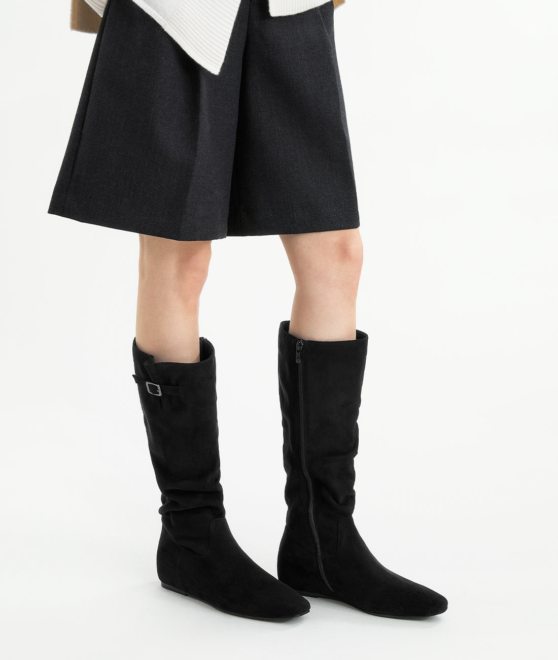 Side view of a woman wearing the black suede slouch boots with a side buckle, showing the slouching shaft and hidden lift